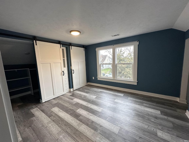 unfurnished bedroom featuring a textured ceiling, a barn door, wood-type flooring, and vaulted ceiling