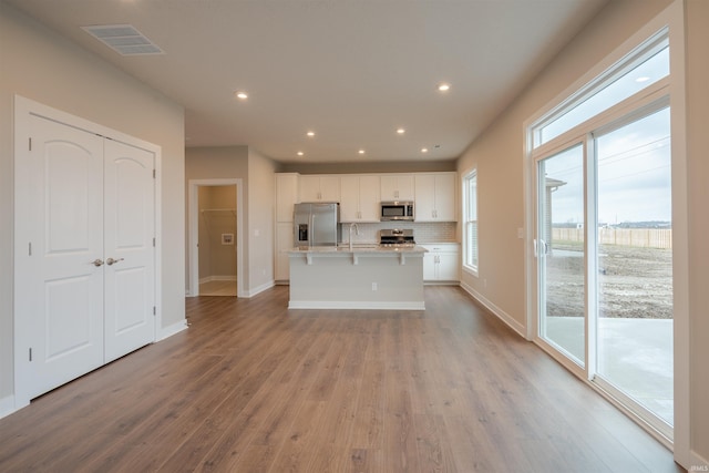 kitchen featuring a center island with sink, white cabinets, decorative backsplash, light wood-type flooring, and stainless steel appliances