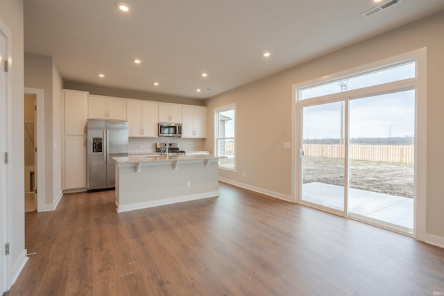 kitchen featuring decorative backsplash, light stone counters, stainless steel appliances, a center island with sink, and white cabinets