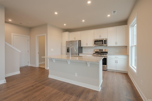 kitchen with a kitchen island with sink, sink, appliances with stainless steel finishes, light stone counters, and white cabinetry