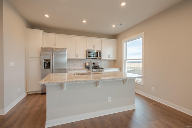 kitchen with white cabinets, appliances with stainless steel finishes, light stone counters, and an island with sink