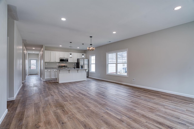 kitchen with appliances with stainless steel finishes, pendant lighting, white cabinetry, light hardwood / wood-style flooring, and a kitchen island