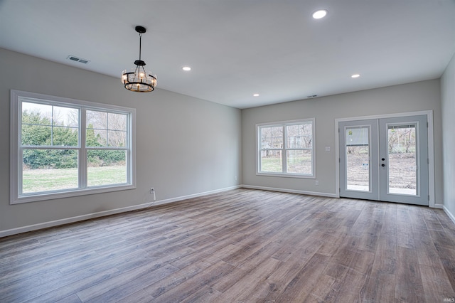 unfurnished room featuring a chandelier, french doors, light wood-type flooring, and a wealth of natural light