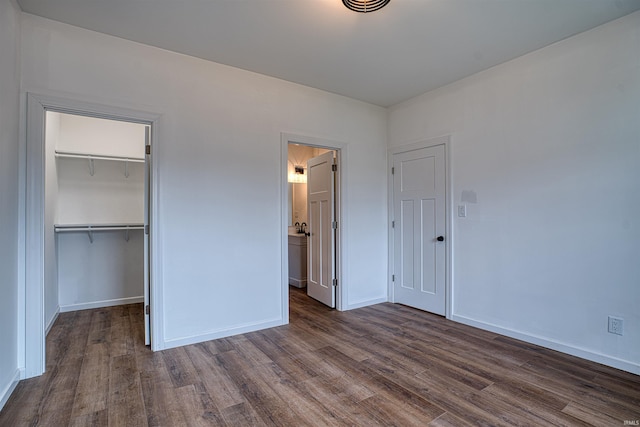 unfurnished bedroom featuring a walk in closet, a closet, and dark hardwood / wood-style floors