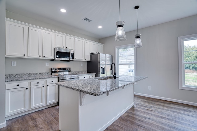 kitchen with white cabinets, sink, decorative light fixtures, light stone counters, and stainless steel appliances