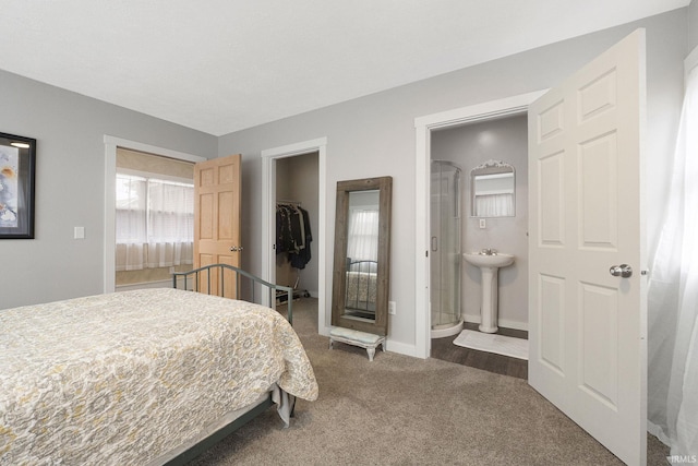 bedroom with a walk in closet, ensuite bathroom, dark carpet, sink, and a closet