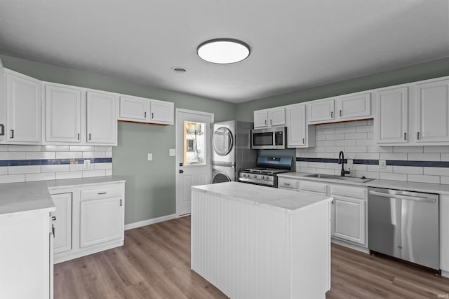 kitchen with appliances with stainless steel finishes, sink, white cabinetry, a kitchen island, and stacked washer / drying machine