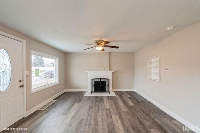 unfurnished living room with ceiling fan, built in features, dark hardwood / wood-style floors, and a textured ceiling