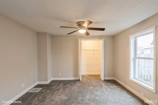 unfurnished bedroom featuring carpet flooring, a walk in closet, a textured ceiling, ceiling fan, and a closet