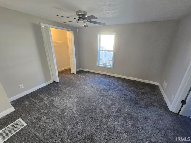 unfurnished bedroom with dark colored carpet, ceiling fan, a walk in closet, and a closet