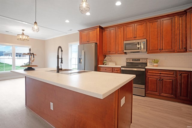 kitchen featuring sink, hanging light fixtures, stainless steel appliances, tasteful backsplash, and an island with sink