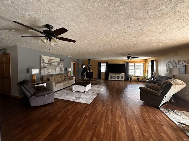 living room with a textured ceiling, ceiling fan, a wood stove, and dark wood-type flooring