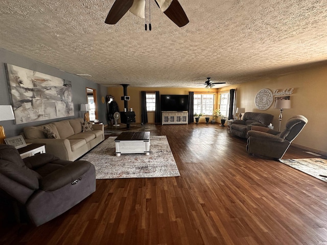 living room with ceiling fan, dark hardwood / wood-style flooring, a wood stove, and a textured ceiling