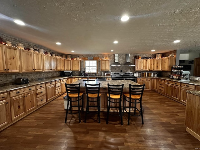 kitchen featuring a kitchen breakfast bar, a kitchen island with sink, dark wood-type flooring, and wall chimney range hood