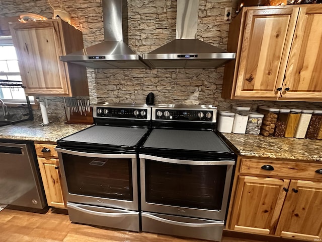 kitchen with stone counters, decorative backsplash, wall chimney range hood, and appliances with stainless steel finishes