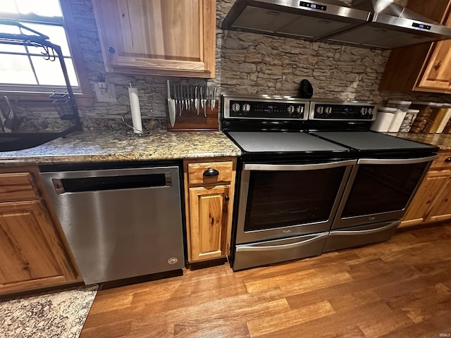 kitchen featuring exhaust hood, sink, light hardwood / wood-style flooring, dark stone countertops, and appliances with stainless steel finishes