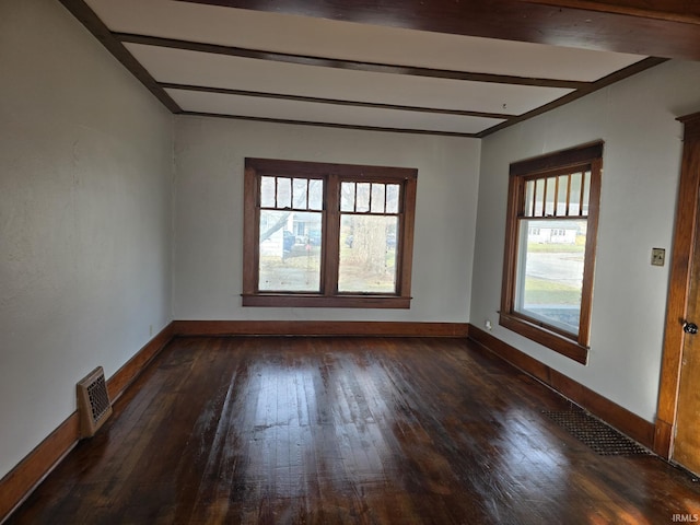 spare room featuring beam ceiling, dark wood-type flooring, and a healthy amount of sunlight