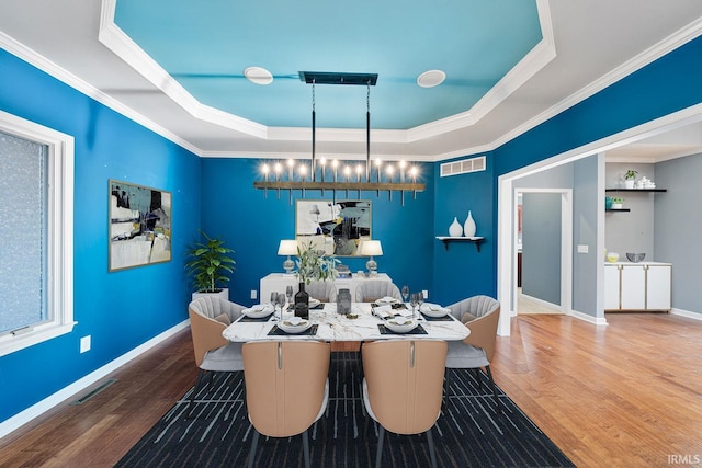 dining space featuring a raised ceiling, wood-type flooring, and ornamental molding