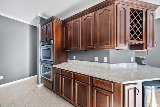 kitchen with light stone counters, ornamental molding, dark brown cabinets, stainless steel double oven, and light tile patterned floors