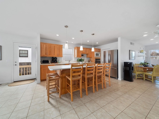 kitchen with a center island, light tile patterned floors, stainless steel fridge, decorative light fixtures, and white microwave