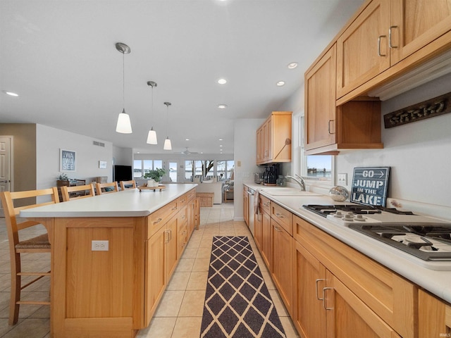 kitchen featuring a kitchen bar, white gas stovetop, sink, pendant lighting, and a kitchen island