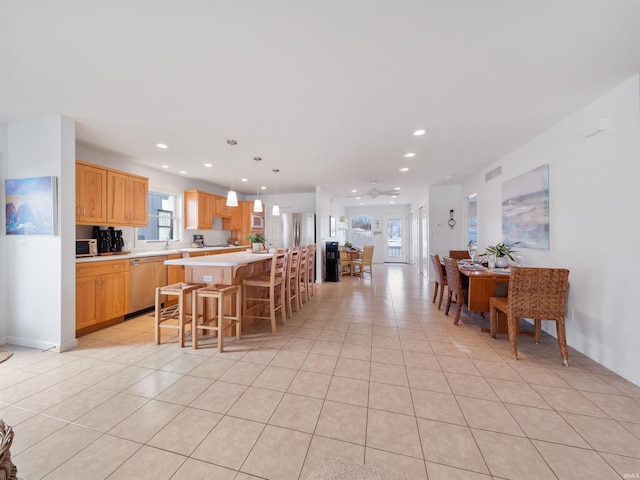 kitchen with a center island, hanging light fixtures, a breakfast bar area, light tile patterned floors, and appliances with stainless steel finishes