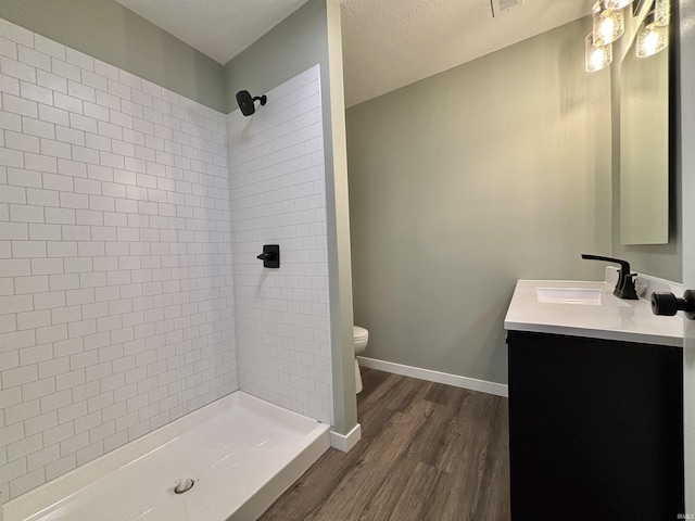 bathroom with vanity, hardwood / wood-style flooring, toilet, tiled shower, and a textured ceiling