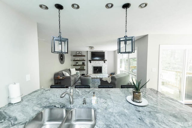 kitchen with decorative light fixtures, a stone fireplace, light stone countertops, and sink