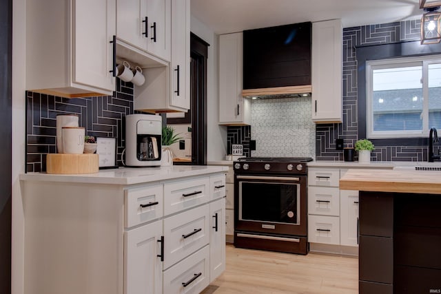 kitchen with white cabinets, custom exhaust hood, range, and backsplash