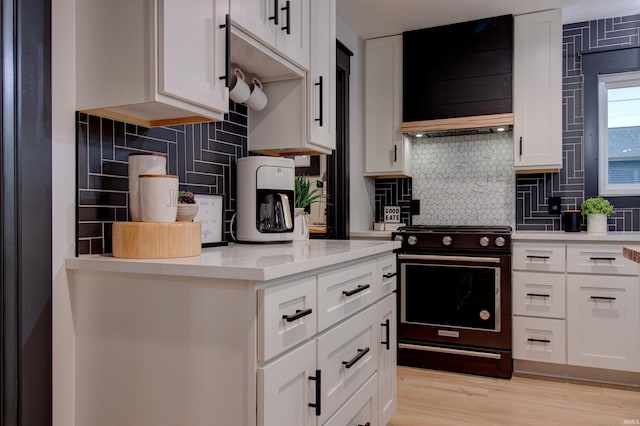 kitchen with white cabinets, custom exhaust hood, stove, and backsplash