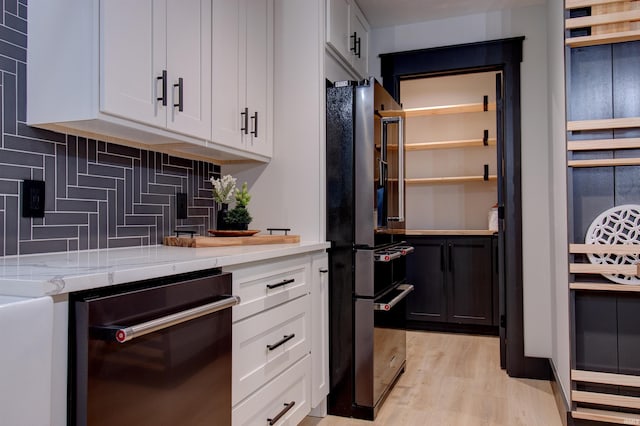 interior space with black appliances, light hardwood / wood-style flooring, decorative backsplash, light stone countertops, and white cabinetry