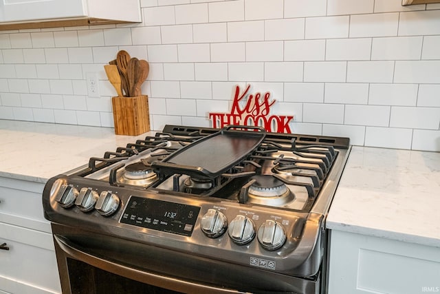 room details featuring backsplash, white cabinets, light stone counters, and gas range oven