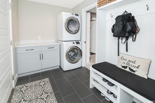 laundry room with cabinets, dark tile patterned flooring, and stacked washer / dryer