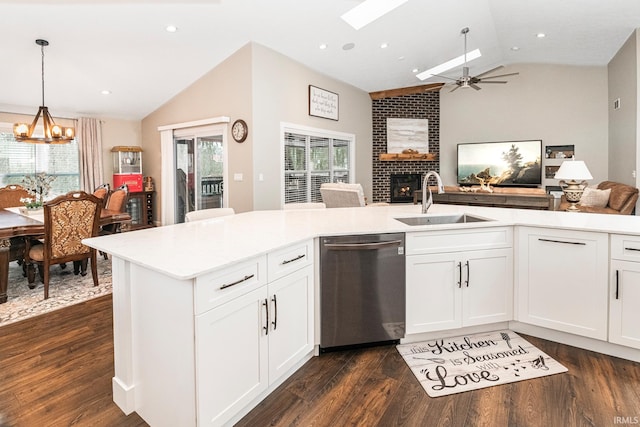 kitchen featuring a brick fireplace, stainless steel dishwasher, vaulted ceiling, sink, and white cabinets