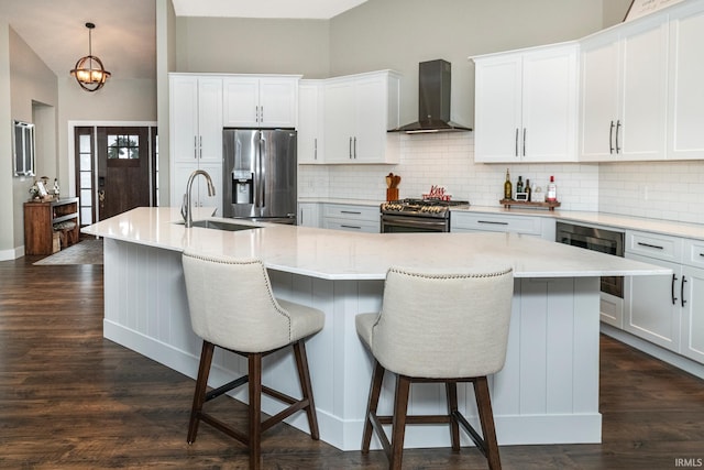 kitchen featuring sink, an island with sink, stainless steel appliances, and wall chimney range hood