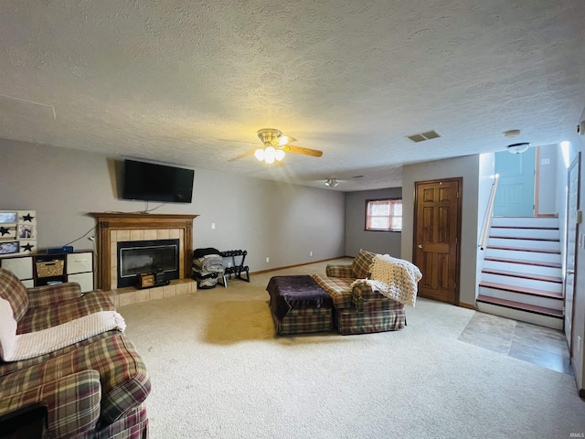 living room featuring a tile fireplace, a textured ceiling, carpet floors, and ceiling fan