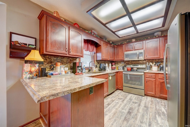 kitchen featuring sink, kitchen peninsula, light hardwood / wood-style floors, decorative backsplash, and appliances with stainless steel finishes