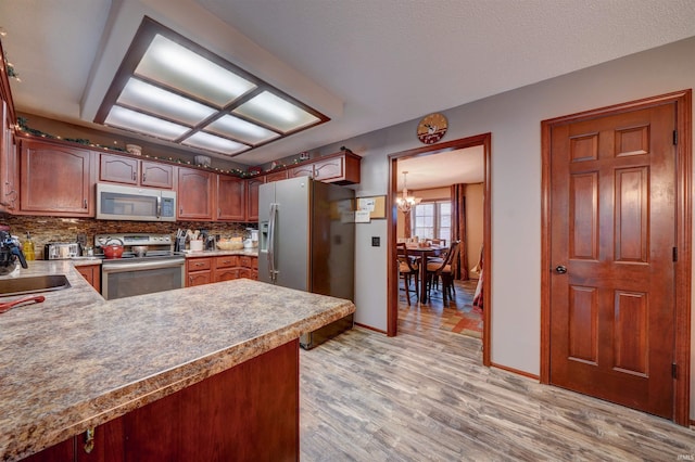 kitchen featuring an inviting chandelier, kitchen peninsula, decorative backsplash, appliances with stainless steel finishes, and light wood-type flooring