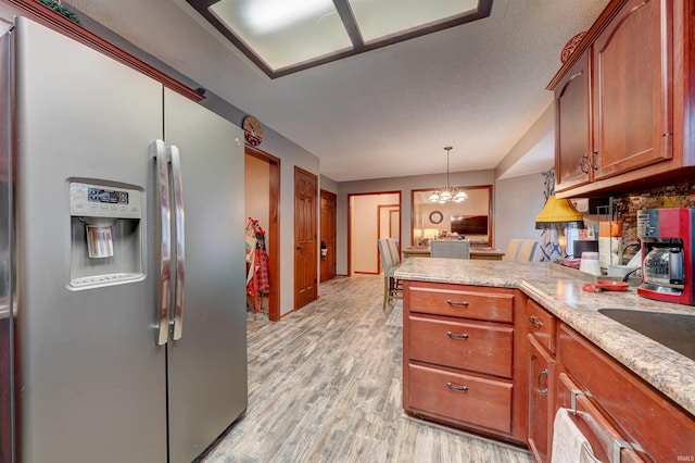 kitchen featuring kitchen peninsula, stainless steel refrigerator with ice dispenser, pendant lighting, an inviting chandelier, and light hardwood / wood-style floors