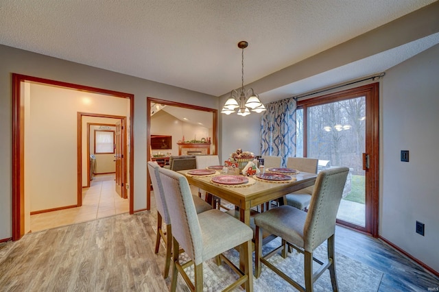 dining room with vaulted ceiling, light wood-type flooring, a textured ceiling, and a chandelier