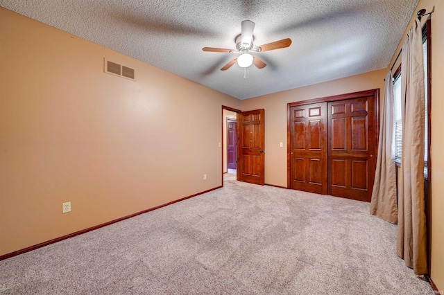 unfurnished bedroom with ceiling fan, a closet, light carpet, and a textured ceiling