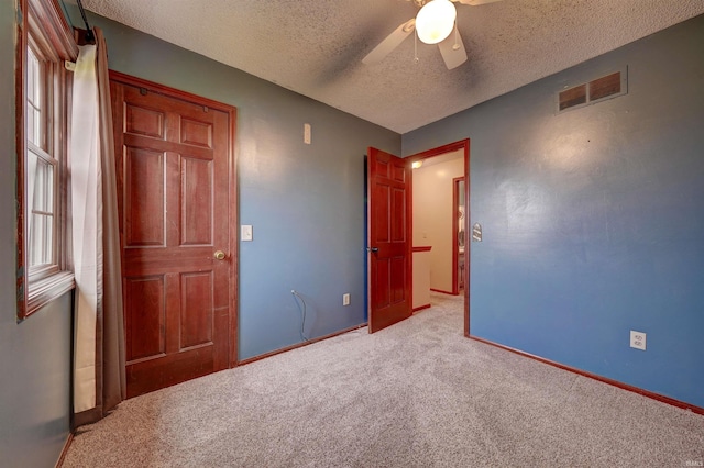 unfurnished bedroom with ceiling fan, light colored carpet, and a textured ceiling