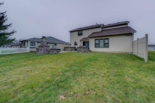 rear view of house with a lawn, a fireplace, and a hot tub