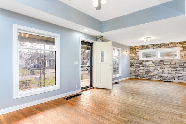 interior space with a tray ceiling, ceiling fan, and light wood-type flooring