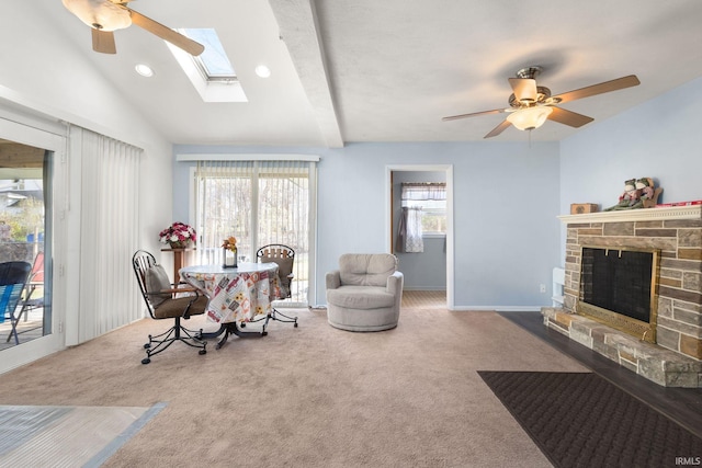 dining area featuring carpet flooring, lofted ceiling with skylight, ceiling fan, and a stone fireplace