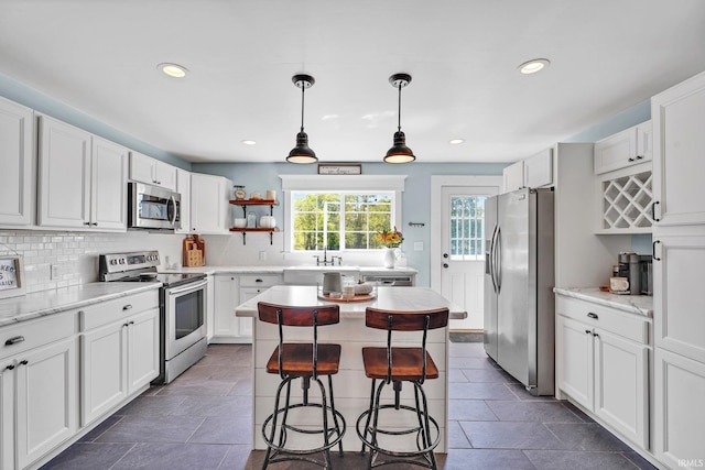 kitchen featuring backsplash, stainless steel appliances, white cabinets, hanging light fixtures, and a breakfast bar area