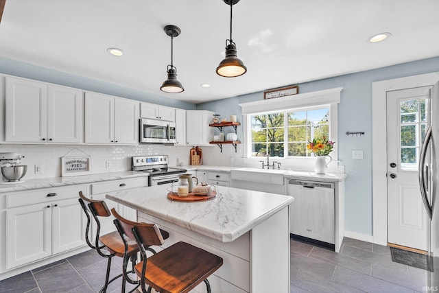 kitchen featuring pendant lighting, backsplash, appliances with stainless steel finishes, a kitchen bar, and white cabinetry