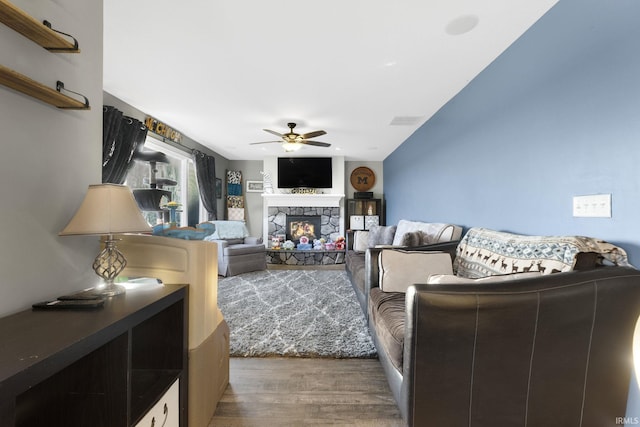 living room with a stone fireplace, ceiling fan, and hardwood / wood-style floors