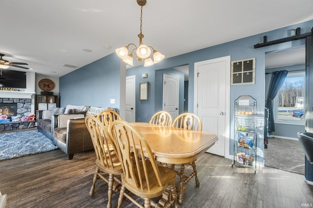 dining space featuring a fireplace, dark wood-type flooring, and ceiling fan with notable chandelier