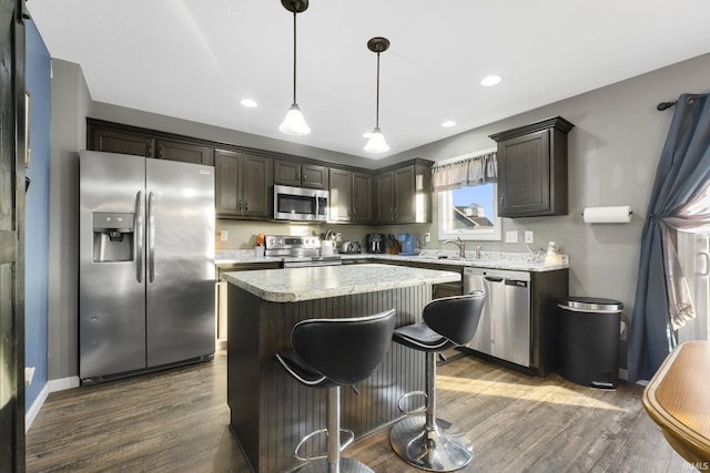 kitchen with appliances with stainless steel finishes, dark brown cabinets, dark hardwood / wood-style floors, a kitchen island, and hanging light fixtures